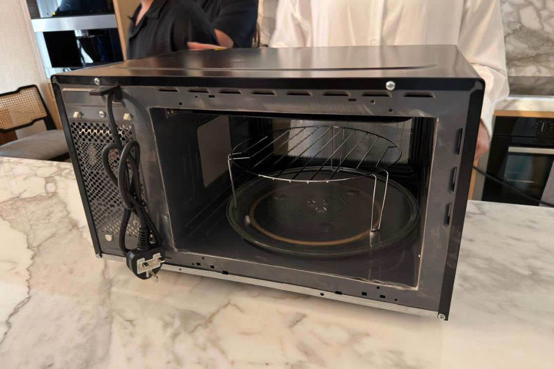 Technician inspecting an open microwave oven during repair service in Dubai.